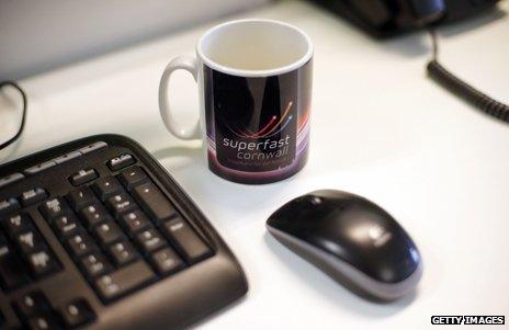 Mug with Superfast Cornwall logo next to a computer