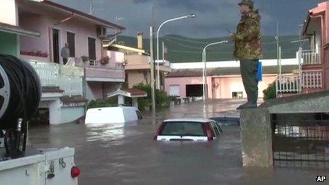 A rescue worker standing on wall overlooking flooded street with submerged cars after a cyclone brought severe flooding to Sardinia