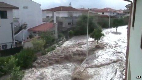 Flood water gushes down a street in Sardinia following a huge rainstorm
