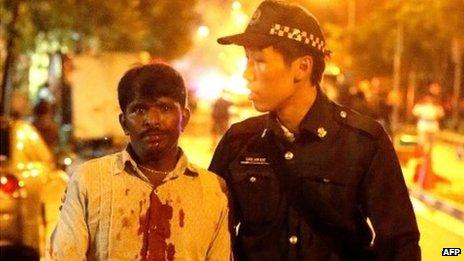 A South Asian man with a blood-spattered shirt is led away by a Singaporean policeman during the riot in Little India