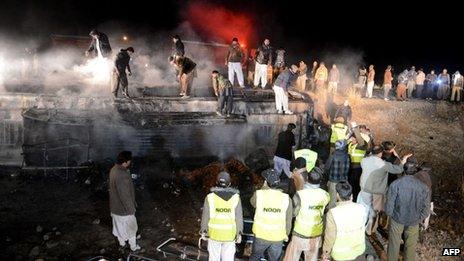 Pakistani rescuers and security personnel gather around a burnt passenger bus carrying Shia pilgrims at the site of a suicide bombing in Akhtarabad, on the outskirts of Quetta, the capital of Balochistan province on 1 January 2014