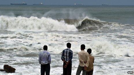 Men watch waves crash on beach in India