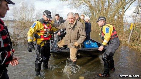 Prince Charles gets out of a boat on a flooded road