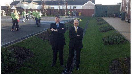 Two men stand in a large ditch next to a school playground