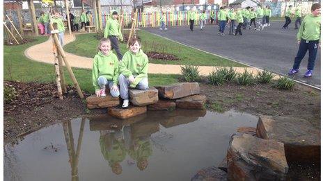 Two children sitting on rocks next to a pond next to a school playground