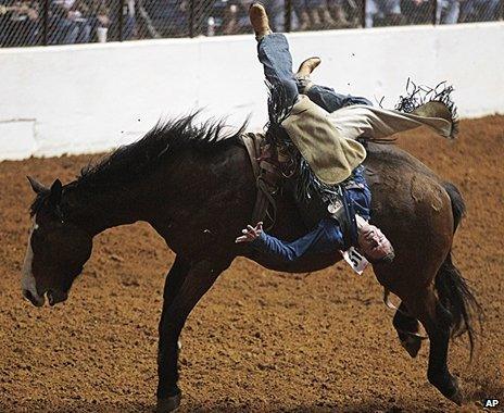 A man is upside down as he is thrown from a bucking horse at a rodeo