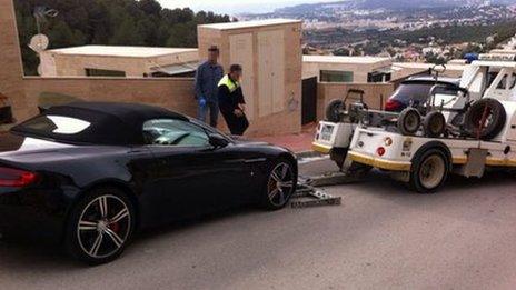 An Aston Martin is towed away from alleged fraudster's home in Barcelona