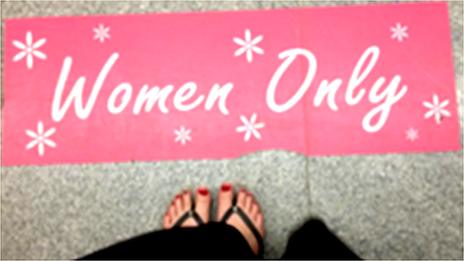 Women in sandals standing before Women Only sign