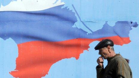 A man walks past a poster in Sevastopol on 13 March 2014 depicting Crimea with the colours of the Russian flag.