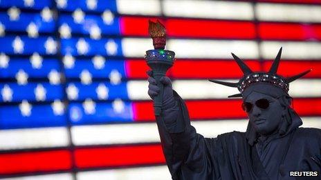 A person dressed up in a Statue of Liberty in front of a US flag