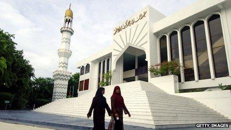Two women walk past mosque