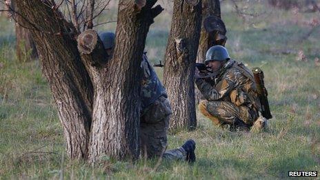 Ukrainian soldiers aim rifles and take cover behind trees as pro-Russia protesters gathered in front of a Ukrainian airbase in Kramatorsk.