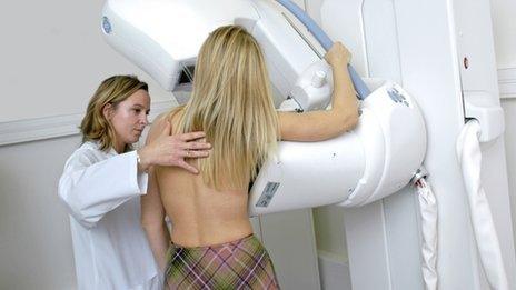 Radiographer preparing a woman for a mammogram