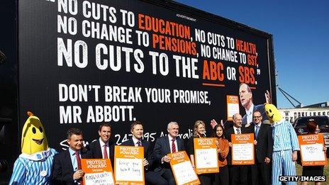 Ministers and Senators pose for media in front of a billboard showing an image of Prime Minister Tony Abbott at a ABC protest rally outside of Parliament House on May 13