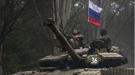 A pro-Russian rebel looks up while ridding on a tank flying Russia's flag, on a road east of Donetsk