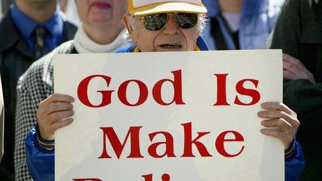 Man holding a sign that says: "God Is Make Believe"