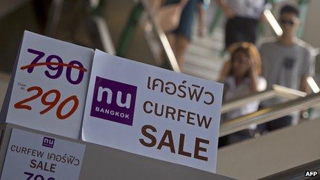 Tourists walk past discount promotion placards displayed at a shop in Bangkok