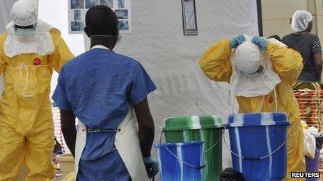 A health worker takes off his protective gear under the surveillance of a colleague at a treatment facility for Ebola victims in Monrovia September 29,
