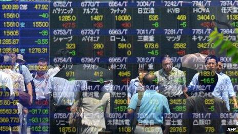 Pedestrians walk past a share prices board of the Tokyo Stock Exchange in Tokyo