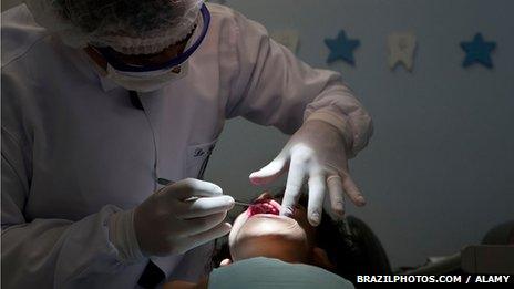 A dentist in Brazil looks into a young girl's mouth