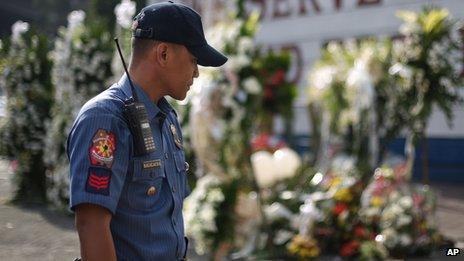A Filipino policeman looks at flowers laid outside the gates of the Philippine National Police headquarters Camp Crame in suburban Quezon city, north of Manila, Philippines, Sunday, Feb. 1, 2015 for the 44 commandos who perished allegedly in a clash with Muslim rebels in Maguindanao, southern Philippines