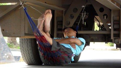 A man sleeps with his hammock underneath a truck