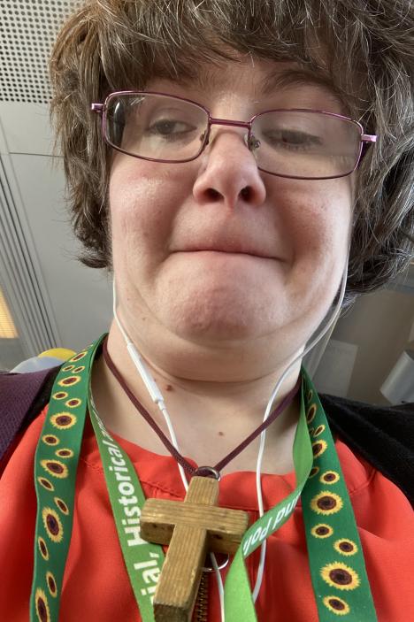 A woman wearing glasses and a green sunflower lanyard, with a wooden cross necklace