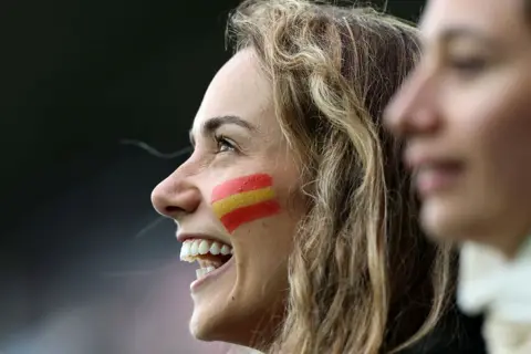 Getty Images Side shot of a young woman laughing with the Spanish flag painted on her cheek 