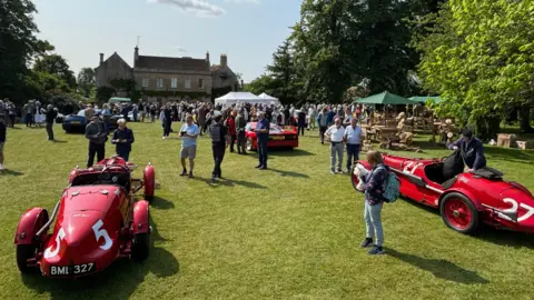 Wiltshire & Bath Air Ambulance Hundreds of visitors in a garden looking at historic cars and talking to each other around picnic benches and a marquee.