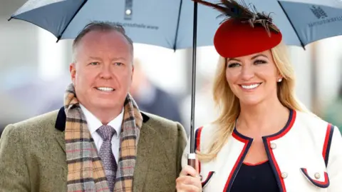 Michelle Mone pictured standing under an umberella next to her husband, Doug Barrowman, attending the Cheltenham Festival in 2019