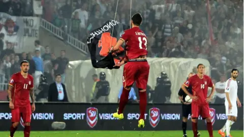 Getty Images Serbia defender Stefan Mitrovic grabs flag suspended from drone on 14 Oct 2014