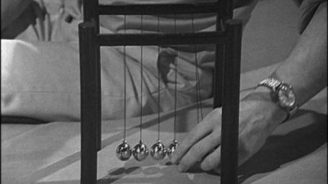 A Newton's cradle, with a hand about to pull back two of the balls.