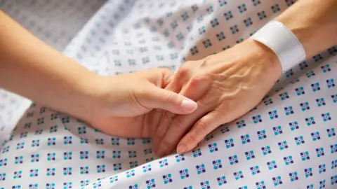 A person holds the hand of someone wearing a hospital gown
