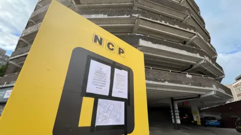 Legal orders posted on a yellow NCP notice board with a multi-storey car park in the background