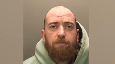 Lincolnshire Police A police mugshot of Samuel Simpkins. He is bald with a light brown beard. He is wearing a green hoodie.