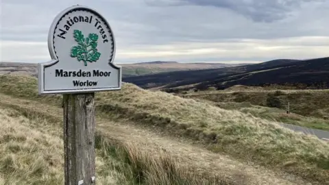 Charles Heslett/BBC A broad moorland landscape with a National Trust sign marking Marsden Moor at Worlaw, set on a wooden post.