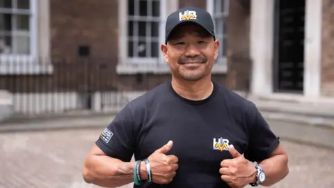 James Manning/PA Wire A man wearing a black hat and t-shirt, smiling with his thumbs up