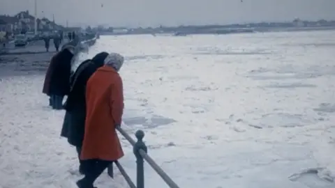 An old photo from 1963 shows people peering over the railings into a sea which is covered in ice. 