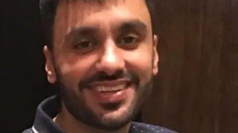 Jagtar Singh Johal, pictured before his arrest, is looking at the camera and smiling. He has short, dark hear and a short beard, and is wearing a navy blue polo shirt.