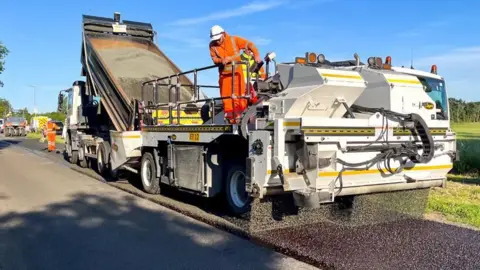 Lincolnshire County Council Worker in orange on top of truck as surface dressing work takes place