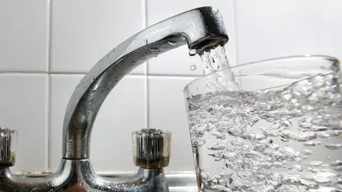 A silver coloured sink beside a glass full of water