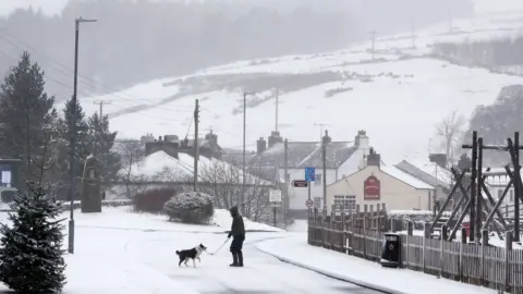 PA Media A man walks his dog through snow in Overwater, Cumbria, as five weather warnings are in place as heavy rain and snow blight swathes of the country on Easter Monday.