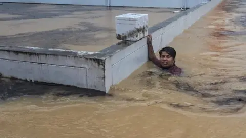 Reuters A man clings to a wall in a flooded street after being swept there while going out to get food supplies in the city of Hat Yai in Thailand