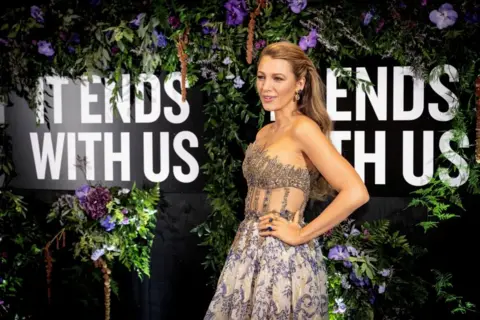 Blake Lively, wearing a silver dress, attends the gala premiere of the movie "It Ends With Us" - with the words of the movie in the background along with flowers