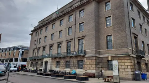 LDRS The Guildhall on the Market Square in Cambridge. Its is a tall building with brown bricks. Bikes are parked outside. 
