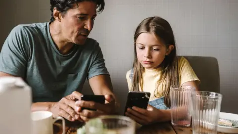 Getty images A stock image of a man and child looking at their phones at the breakfast table