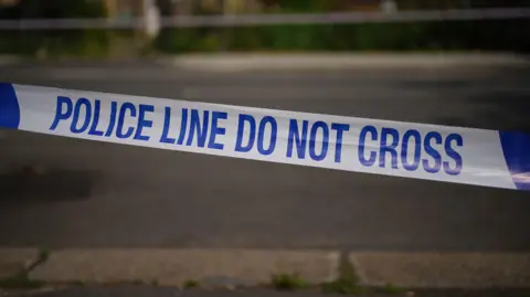 Close-up photo of police tape which says "Police line do not cross' at the scene of an incident on a street. It is blue and white.