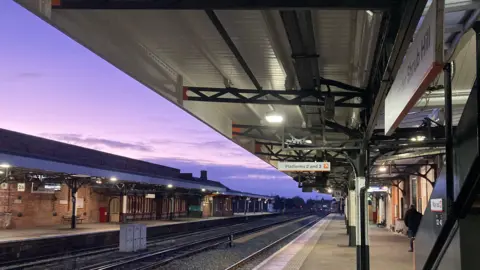 A railway line heading through a railway station. The image is taken from one of the platforms with another platform visible on the other side of the tracks.