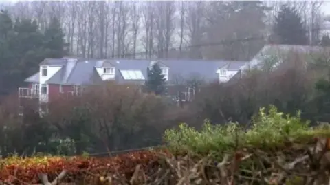 Holmesley Care Home. Photograph taken from distance showing three storey building with red brick exterior.