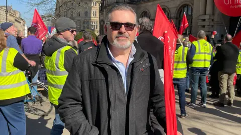 Tom MacDougall/BBC Shane Sweeting, wearing a black jacket and sunglasses.
